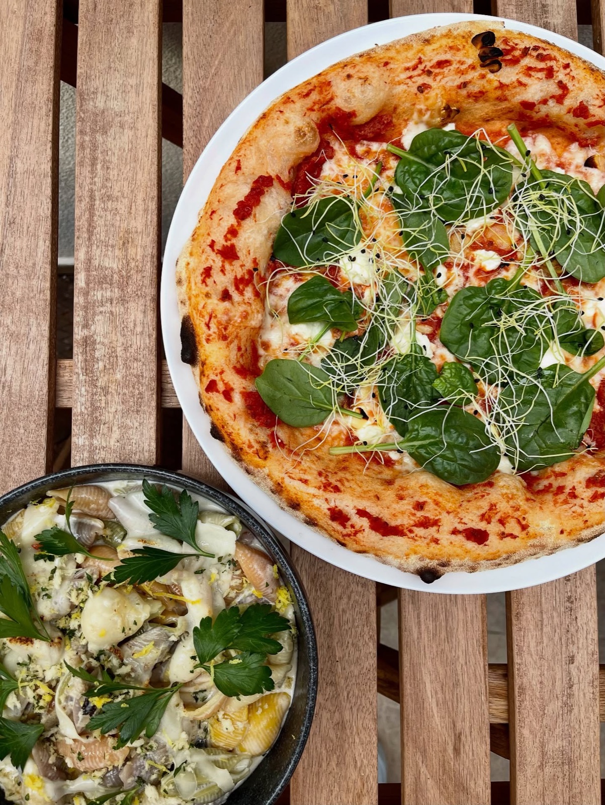 Pizza so špenátom a krémové cestoviny na drevenom stole